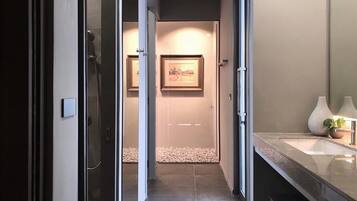 A modern bathroom with a glass shower enclosure, a sink with a vase, and a framed picture on the wall.