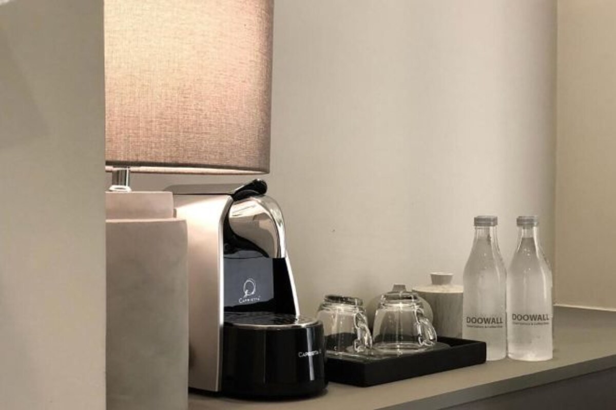 De minibar in een hotelkamer, met een koffieapparaat, twee waterflessen en een glazen bak.