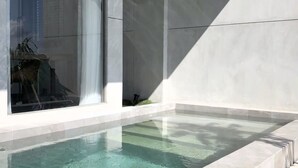 Un área de piscina exterior moderna con cerramiento de vidrio transparente, diseño minimalista y vista panorámica de la ciudad.