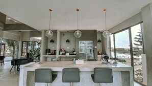 Una cocina moderna con una isla central, luces colgantes y grandes ventanales que ofrecen vistas al exterior.