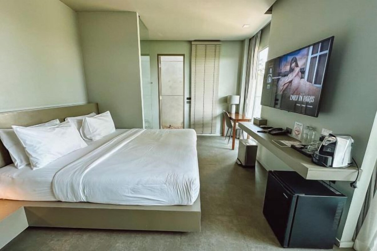 Habitación de hotel con cama, escritorio, televisor y refrigerador.
