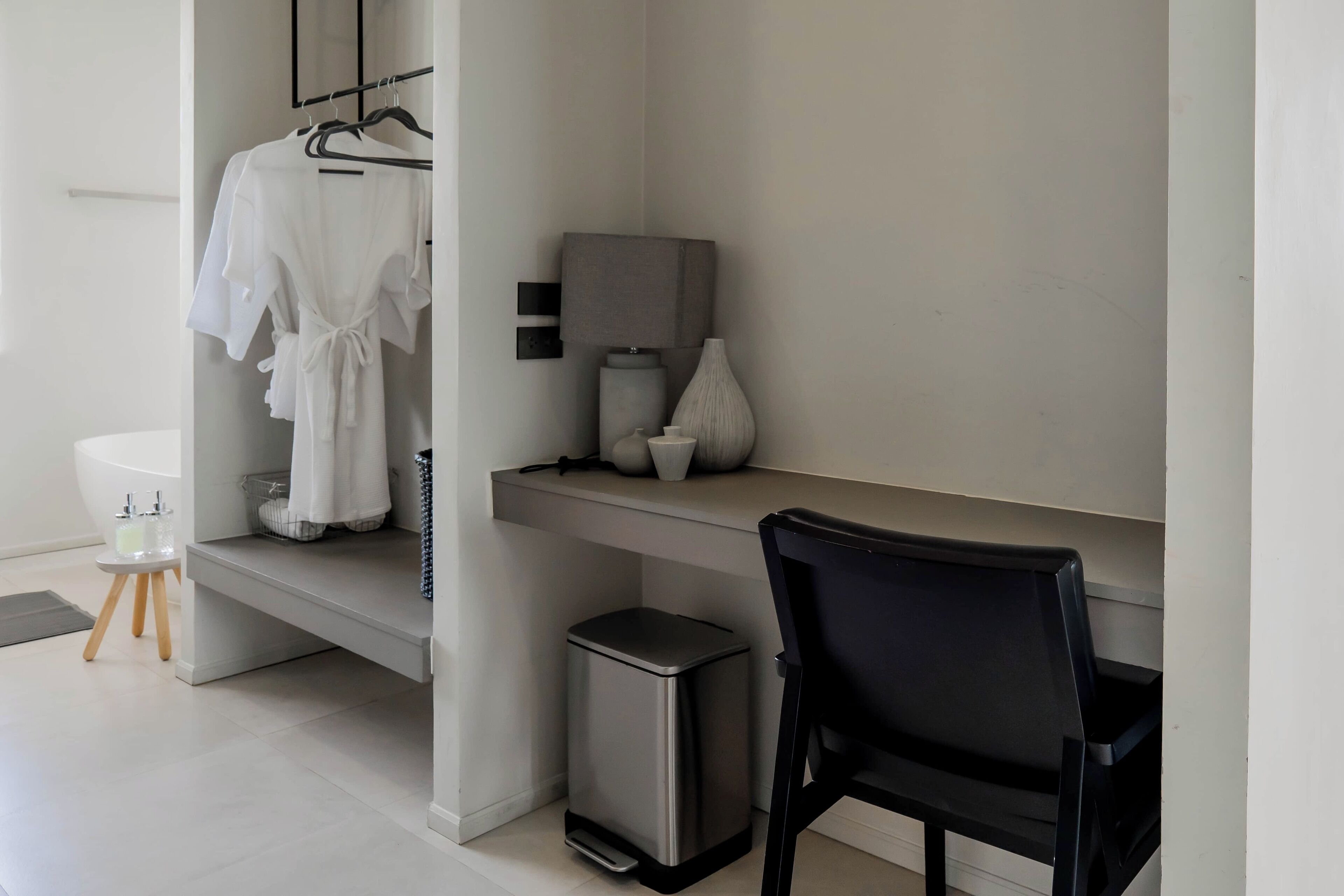 Un baño moderno con una bañera blanca, una silla negra, un taburete pequeño y un cubo de basura.