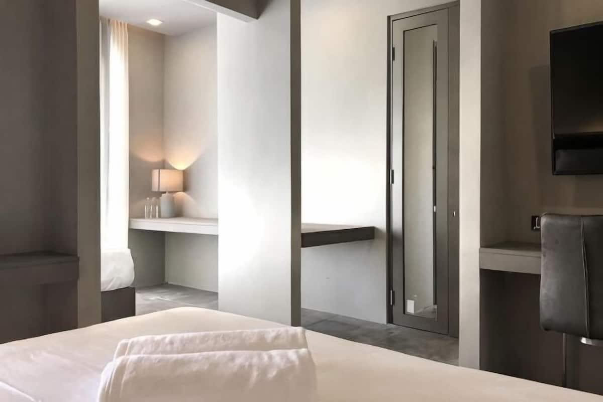 A hotel room with a bed, a mirror, a TV, and a bathroom.