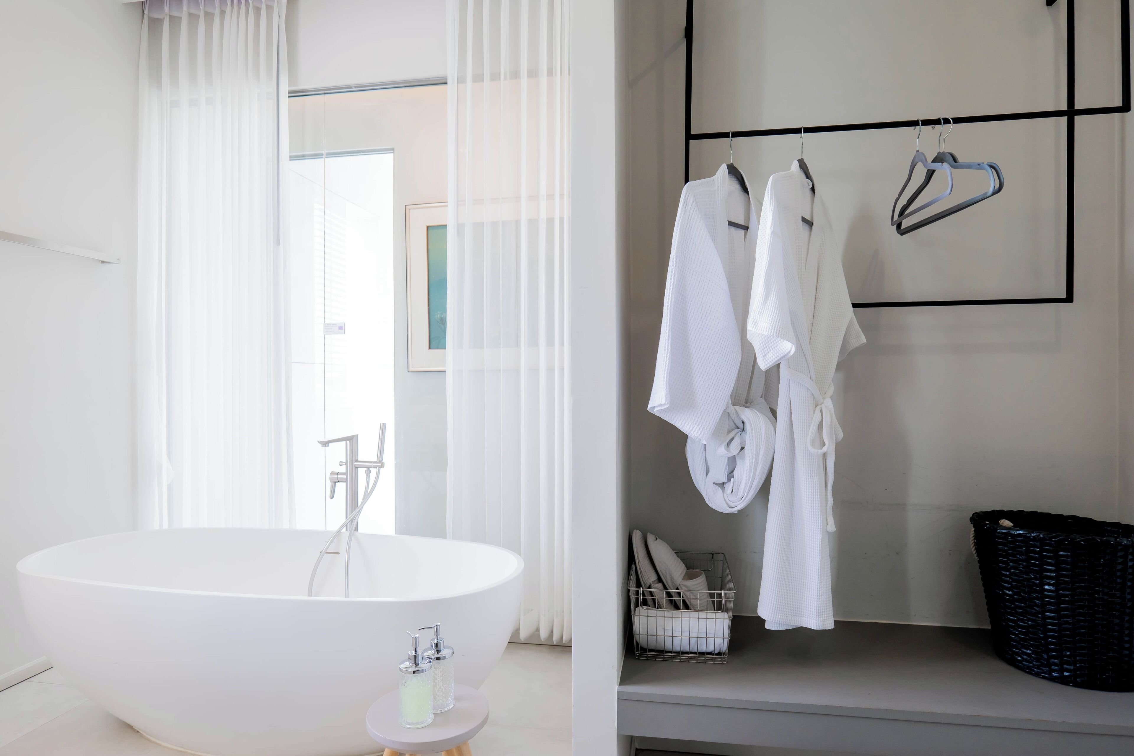 A modern bathroom with a freestanding bathtub, a towel rack with white towels, and a black basket on the floor.