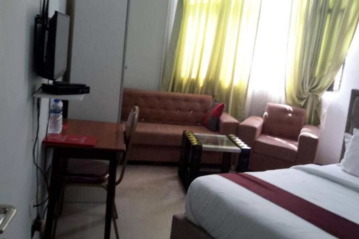 Une chambre d’hôtel comprenant un lit, un canapé, une chaise, une petite table, un téléviseur et une fenêtre avec des rideaux.