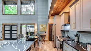 A modern kitchen with a marble countertop, wooden flooring, and a large island. - Luxe Broken Bow Vacation Rental: Hot Tub & Pets OK (Broken Bow)
