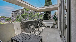 A balcony with a table and chairs, a bathtub, and string lights. - Vibrant Urban Loft in the Core of Little Italy (San Diego)