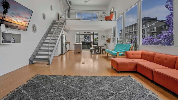A modern apartment with a staircase, a living area with a sofa, a dining area, and a kitchen. - Vibrant Urban Loft in the Core of Little Italy (San Diego)