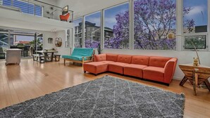 A spacious living area with a large sectional sofa, a teal armchair, and a grey rug. - Vibrant Urban Loft in the Core of Little Italy (San Diego)