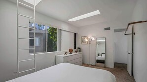 A bedroom with a bed, dresser, mirror, and a window with a view of buildings and trees. - Vibrant Urban Loft in the Core of Little Italy (San Diego)