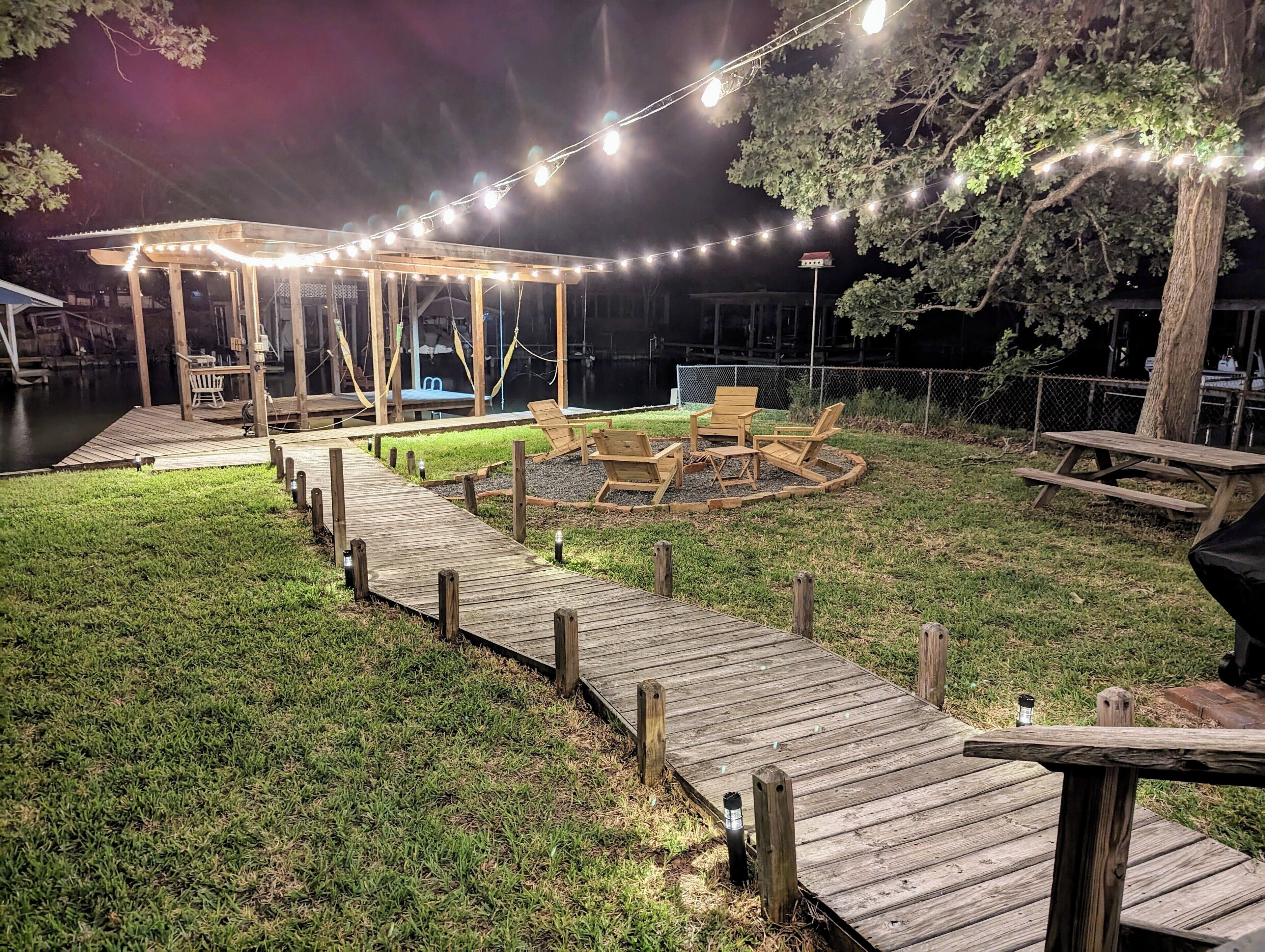 A wooden deck with a gazebo and outdoor seating area, surrounded by a grassy lawn and a body of water.