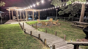 A wooden deck with a gazebo and outdoor seating area, surrounded by a grassy lawn and a body of water.