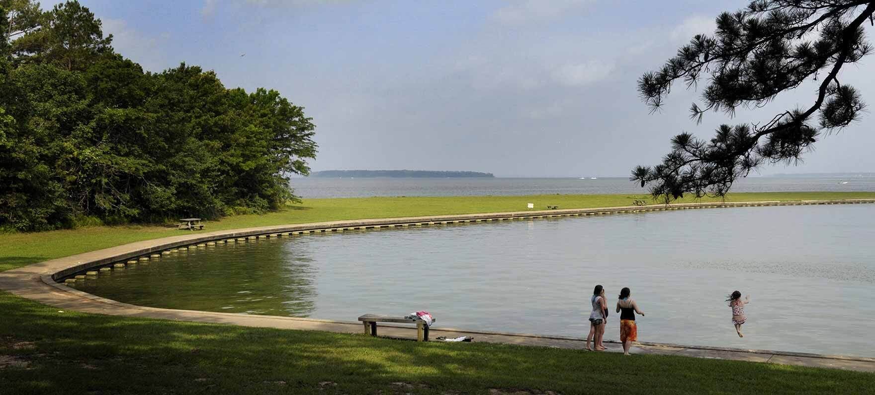 A calm lake with a curved concrete edge, surrounded by grassy areas and trees.