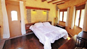 A bedroom with a large bed, wooden beams, a brick accent wall, and a wooden door. - Bahia - spacious family villa with private pool in Moraira (Moraira)