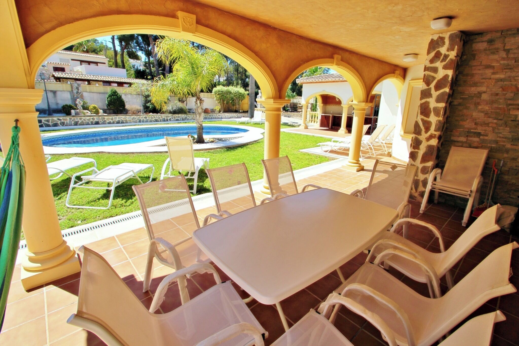 A covered outdoor area with a pool, white chairs, and a table.