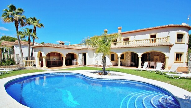 A pool with a curved edge, surrounded by a white building with arches and a tiled roof. - Bahia - spacious family villa with private pool in Moraira (Moraira)