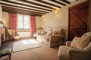 A cozy living room with a fireplace, a sofa set, a striped armchair, and a large wooden door.
