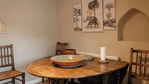 Een eetgedeelte met een ronde houten tafel, stoelen, een schaal en wanddecoratie.