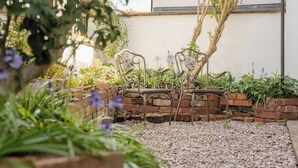 Een tuin met metalen stoelen, een bakstenen muur en een boom.