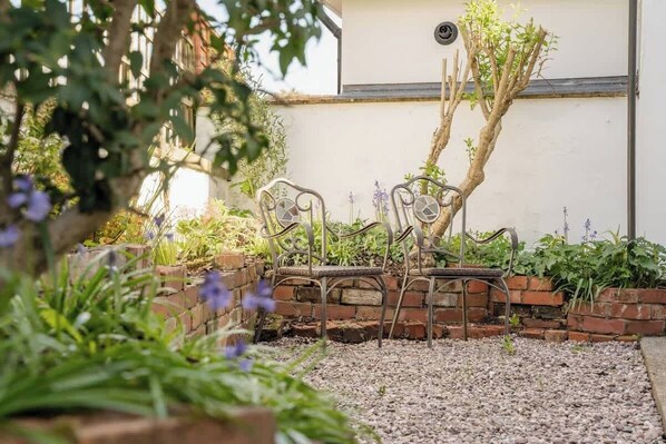A garden with metal chairs, a brick wall, and a tree.