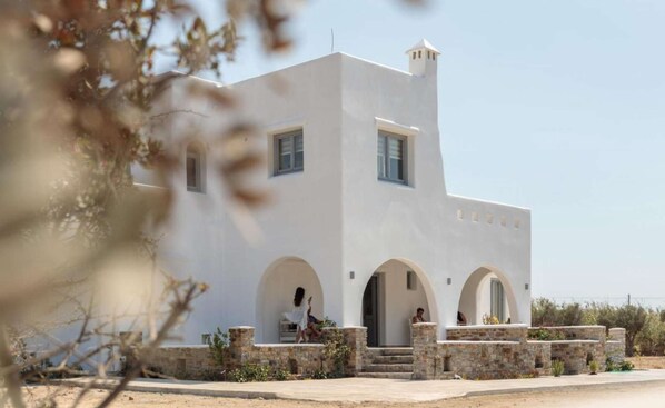A white building with arched doorways and a stone base. - Villa Vaya – Private 180 m² Residence with Jacuzzi and Garden near Agia Anna Beach (Naxos)