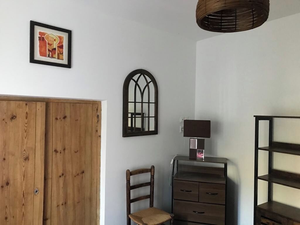 Een kamer met een houten garderobe, een stoel, een bureau met lades, een lamp en een plank.