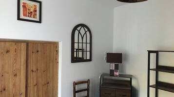 Een kamer met een houten garderobe, een stoel, een bureau met lades, een lamp en een plank.