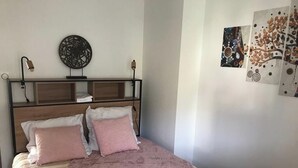 Une chambre à coucher avec un lit, des oreillers, une tête de lit, une lampe fixée au mur et des œuvres d’art.