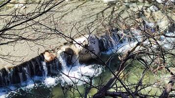 Un élément naturel du paysage, constitué d’une petite cascade, entouré de rochers et de branches.