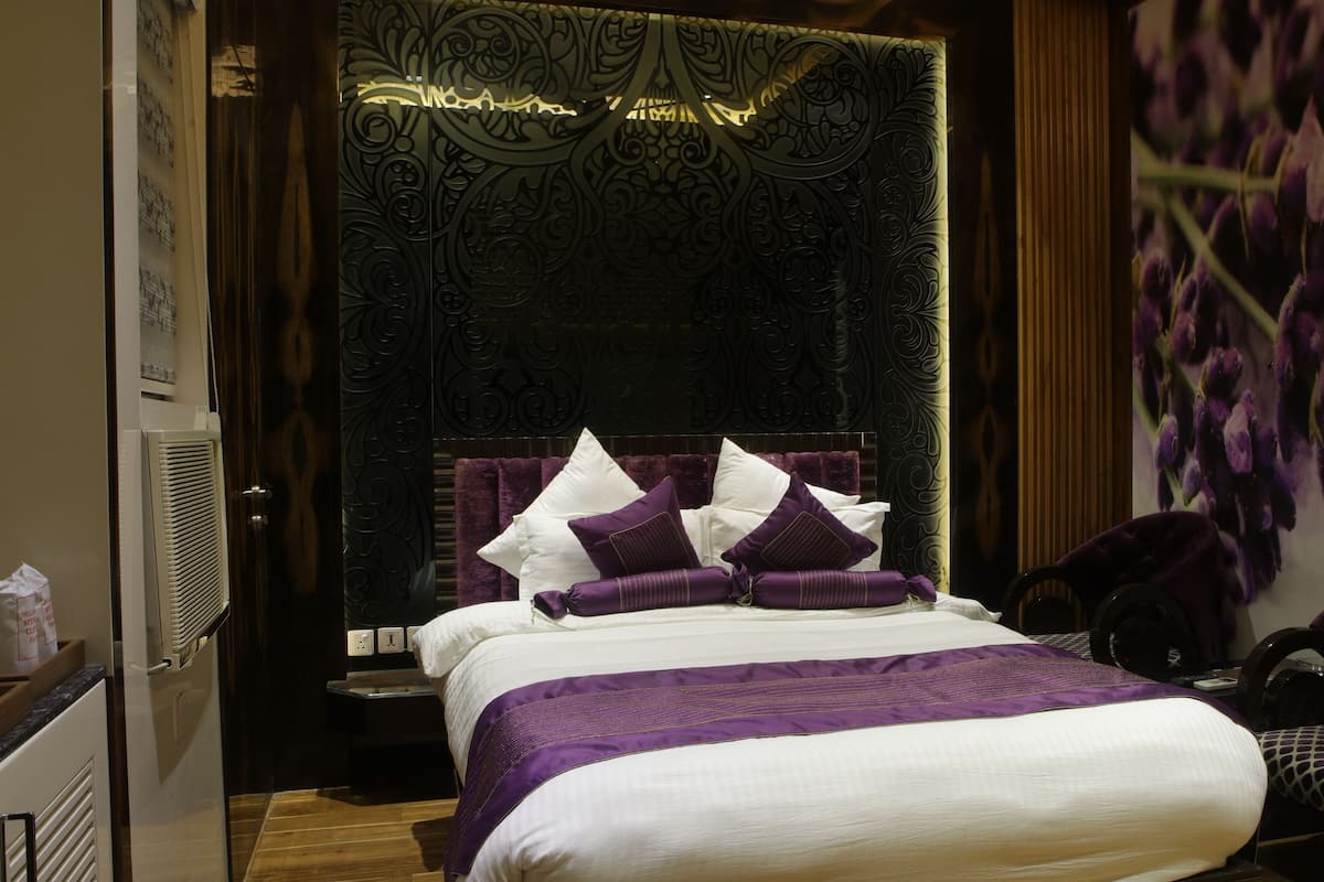 A bedroom with a large bed, a headboard with intricate carvings, and a purple and white color scheme.