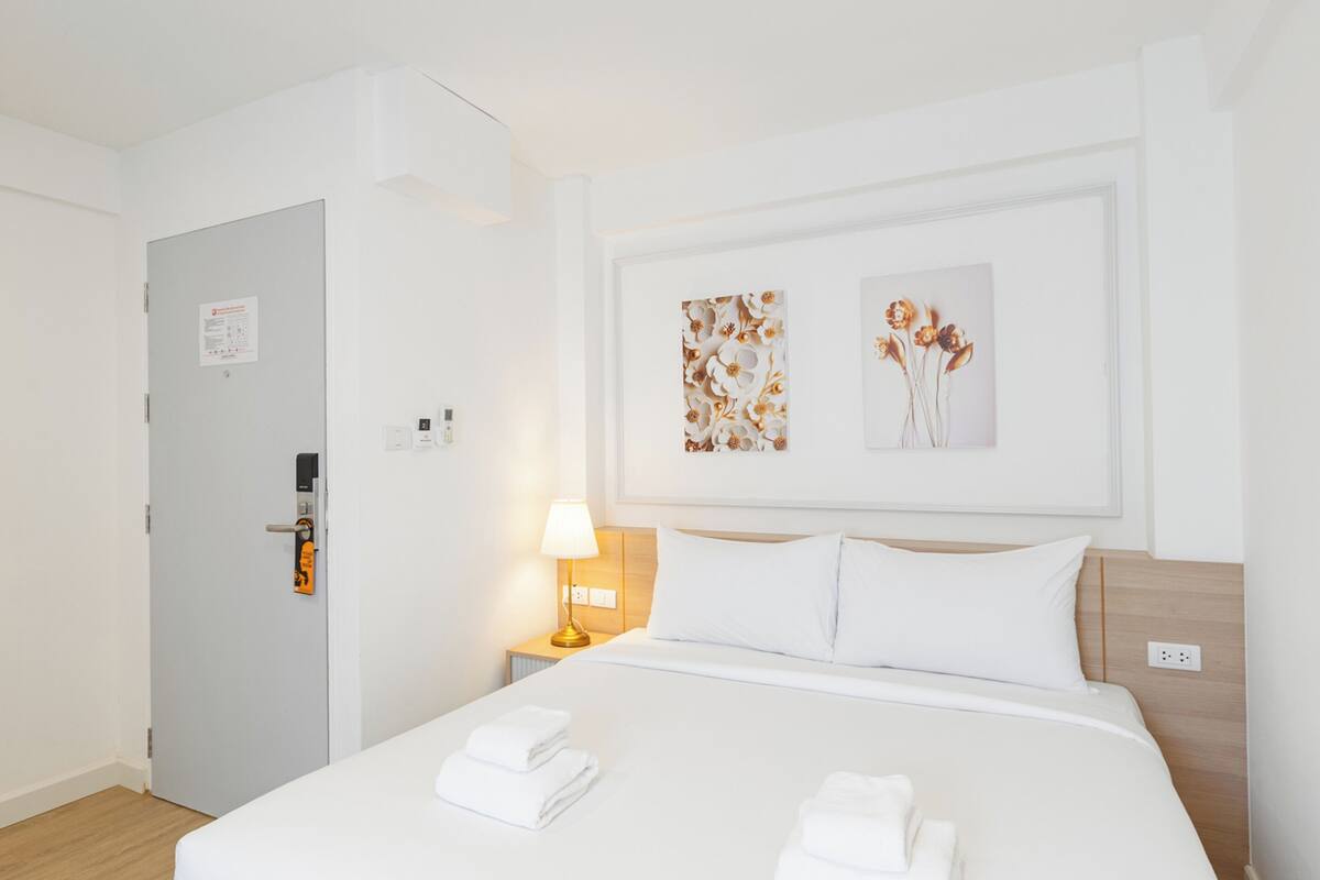 Una habitación de hotel con una cama, dos toallas blancas, una mesita de noche con una lámpara y dos obras de arte floral enmarcadas en la pared.