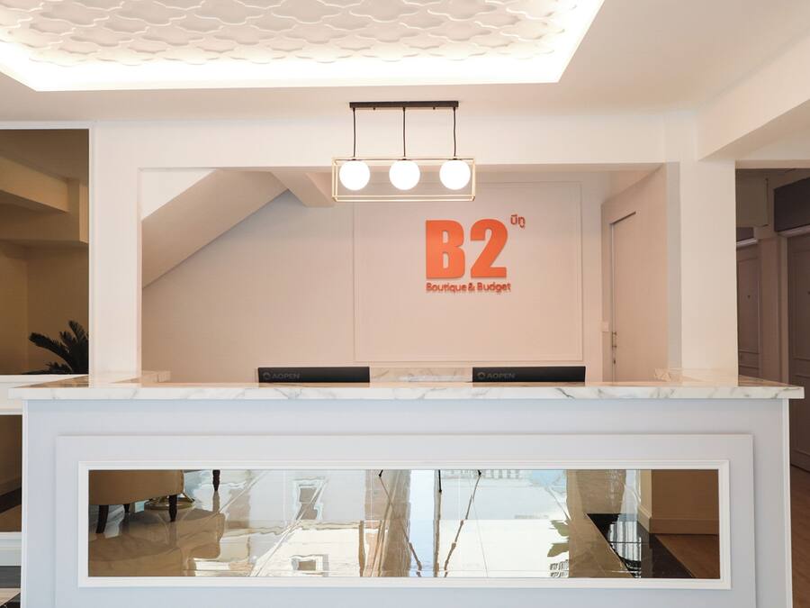 A reception area with a white counter, a ceiling with a wave-like design, and a sign that reads "B2 Boutique & Budget".