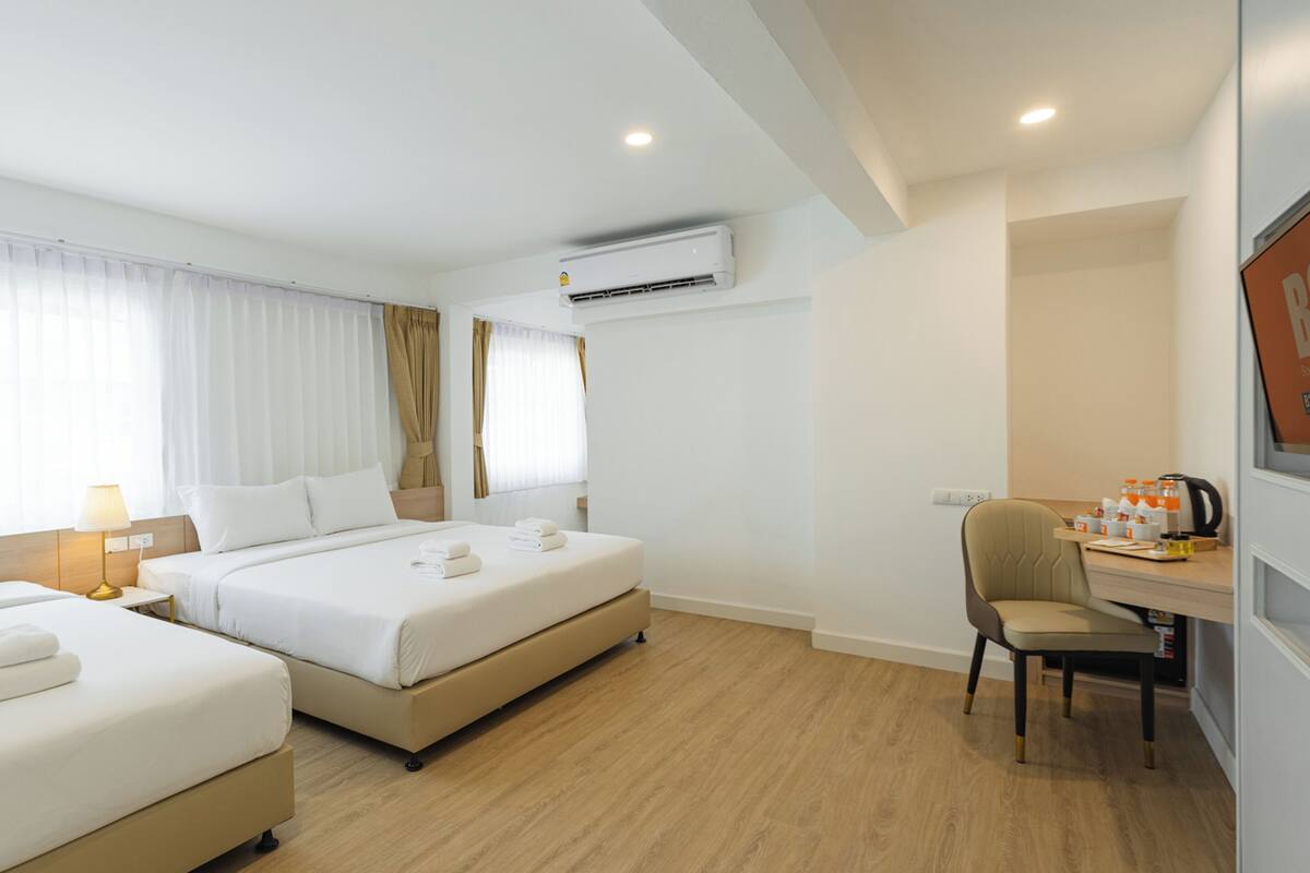 Una habitación de hotel con dos camas, un escritorio, una silla, un aire acondicionado y una ventana con cortinas.