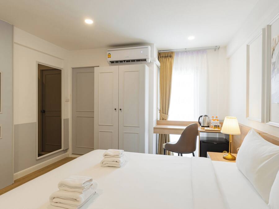 Una habitación de hotel con cama, escritorio, silla, televisor y aire acondicionado.