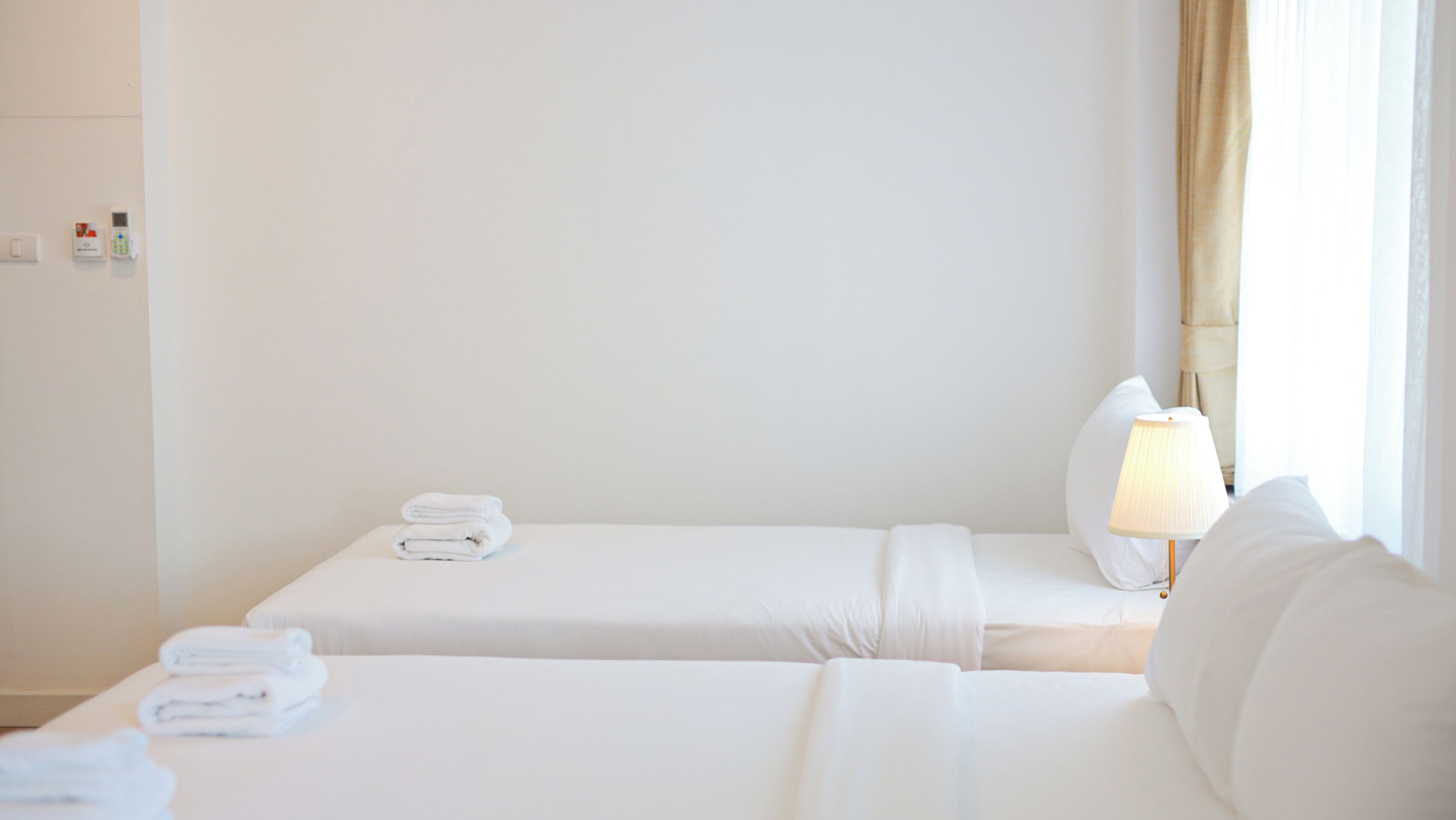 Habitación de hotel con dos camas, una lámpara y un ventanal con cortinas.