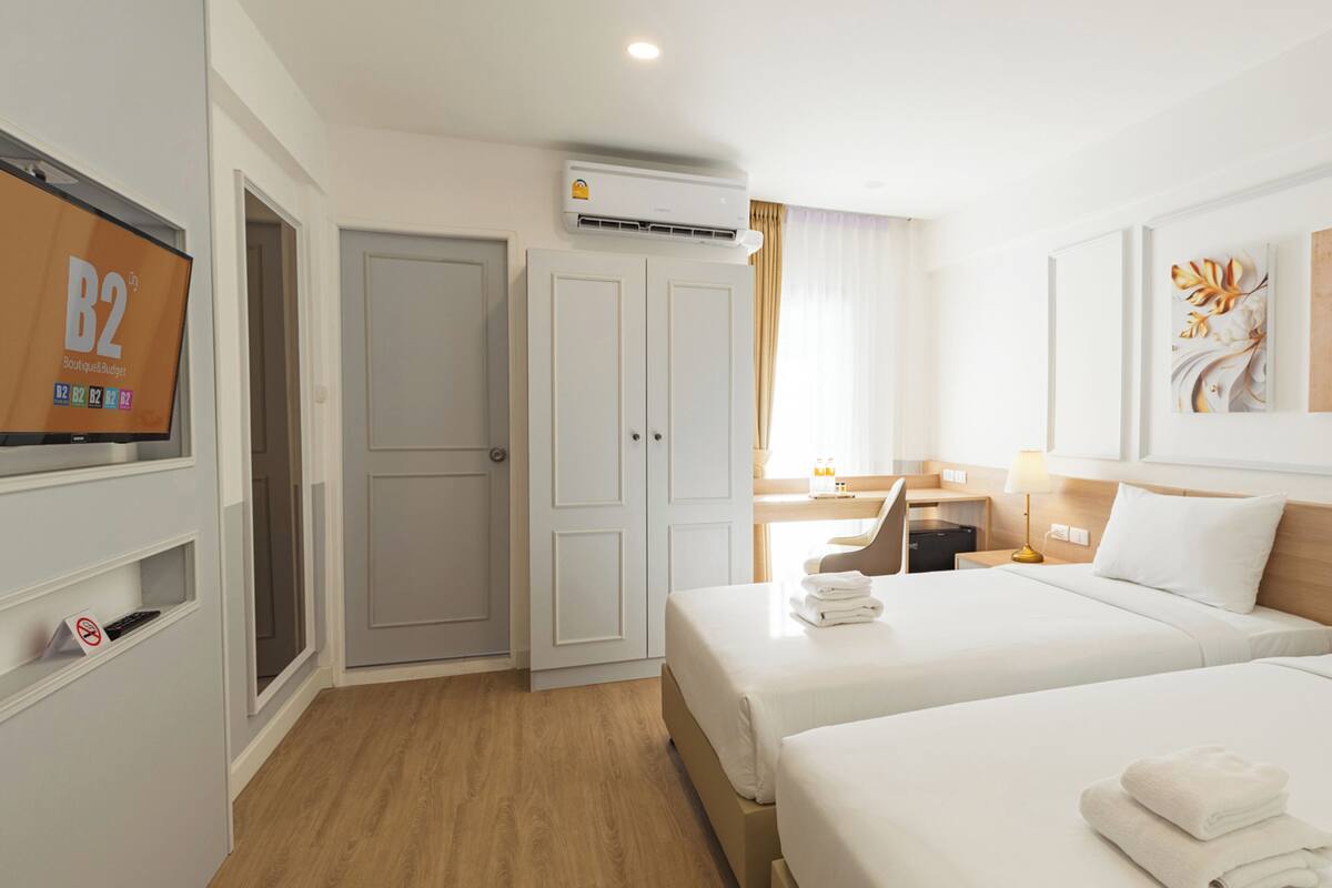 Una habitación de hotel con dos camas, televisión, aire acondicionado y obras de arte en las paredes.