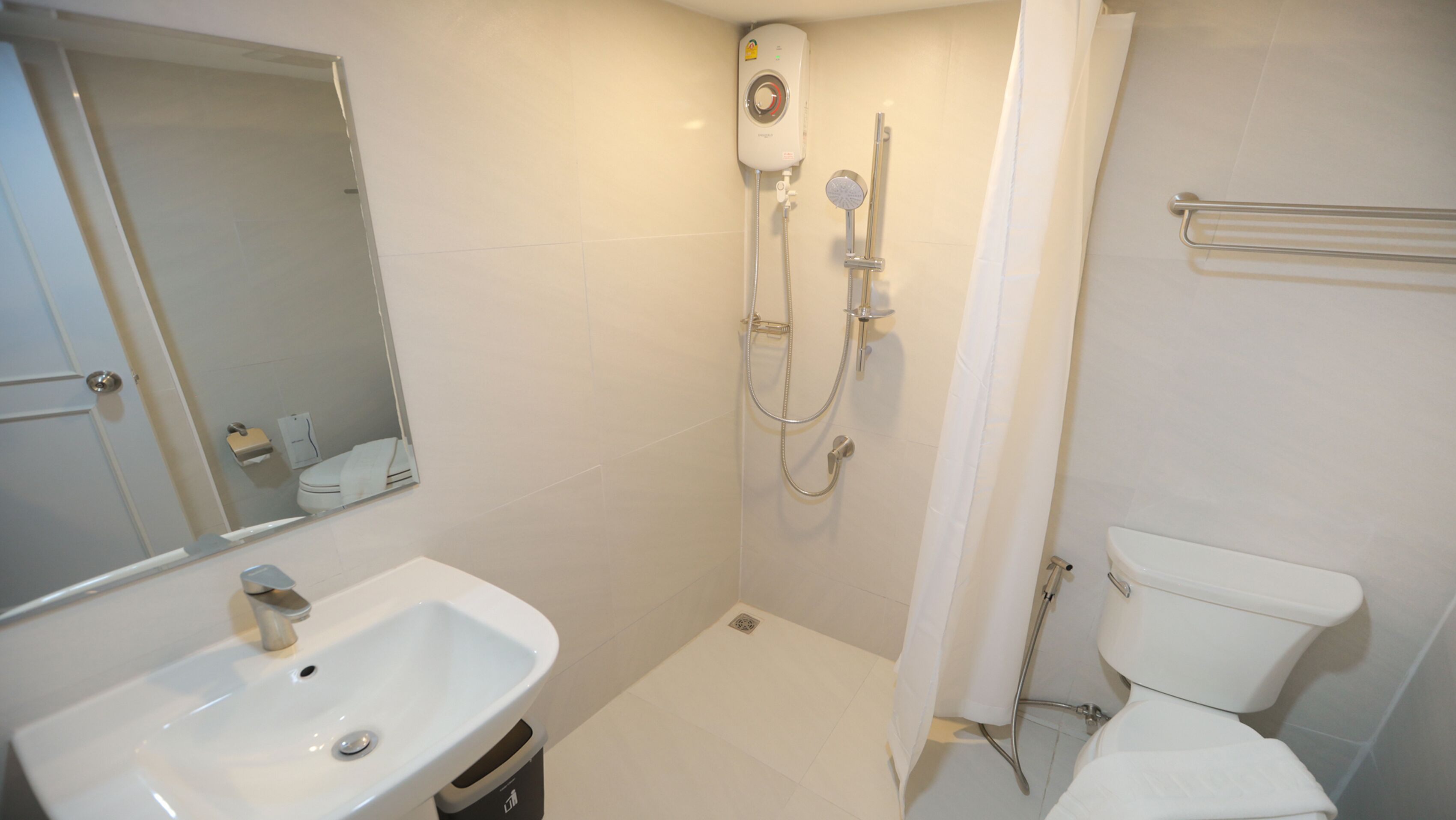 Et badeværelse med vask, toilet, bruser og et håndklædetørrestativ.