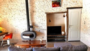 A living room with a stone wall, a fireplace, a television, and a sofa. - Secluded Périgourdine, nestled in the vineyards with a spa and a view (Pomport)