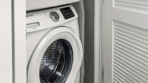 A stacked washer and dryer unit in a laundry room with a door and blinds.