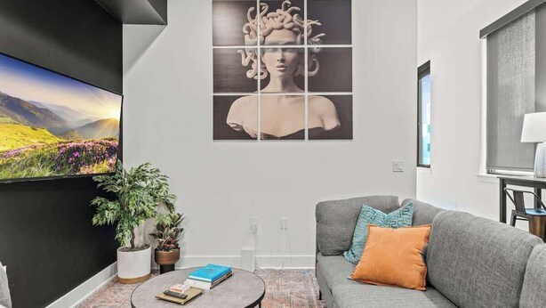 A modern living room with a grey sofa, a round coffee table, and a large painting on the wall.