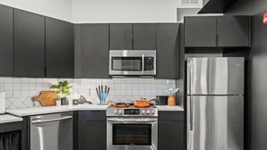 A modern kitchen with dark cabinetry, a stainless steel microwave, oven, and refrigerator.