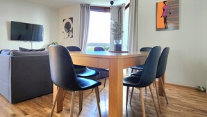 Ein modernes Wohnzimmer mit einem Holzespeisetisch, vier Stühlen, einer Couch, einem Flachbildfernseher und einem fenster mit Vorhängen.