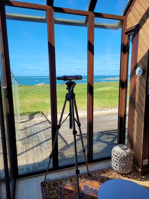 Enjoy the view of the grassy area and sea from this room's large window, where a telescope is set up for stargazing.