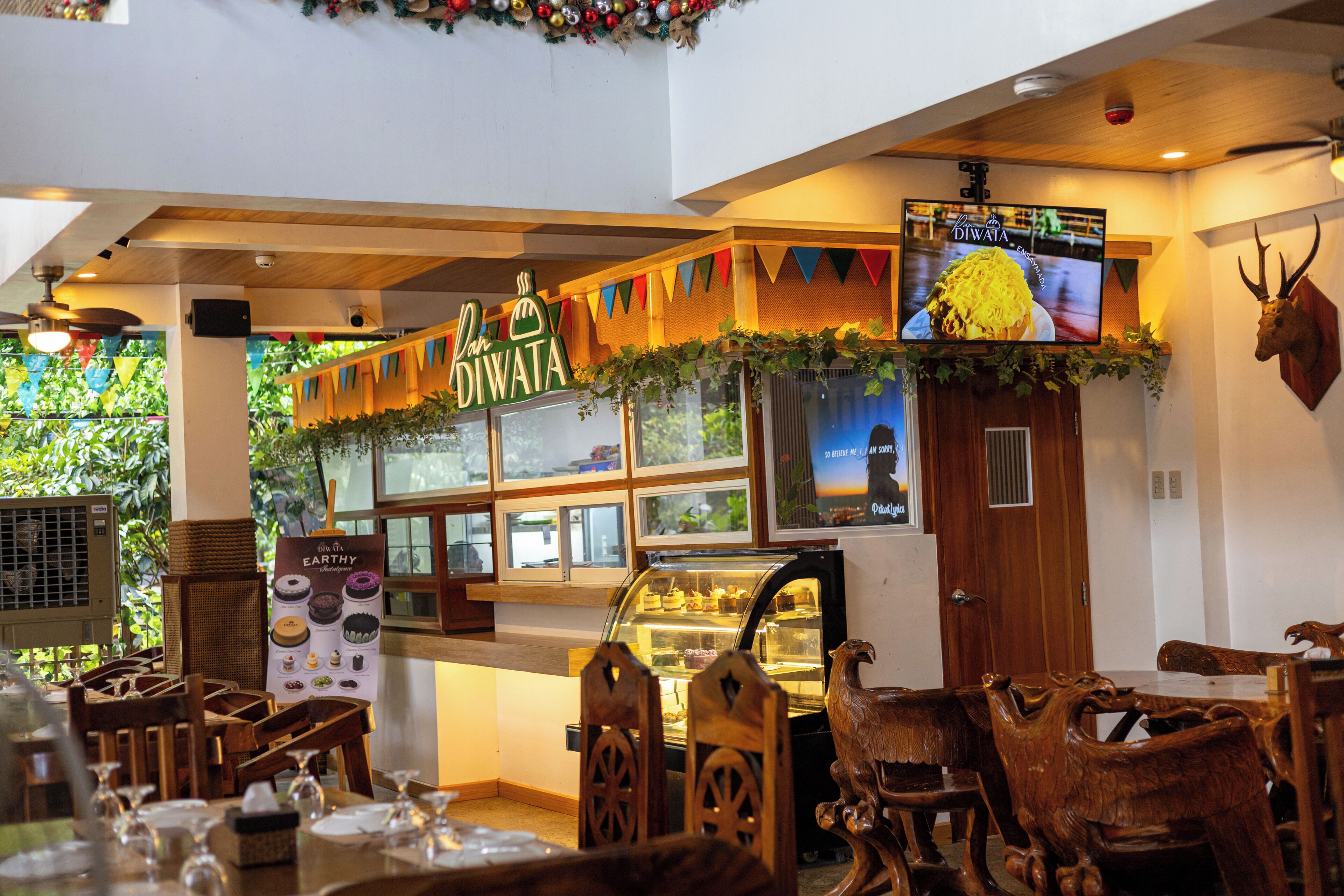 L’intérieur d’un restaurant, avec une salle à manger en bois, un présentoir où sont exposés des produits alimentaires et un écran de télévision.