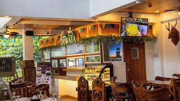 L’intérieur d’un restaurant, avec une salle à manger en bois, un présentoir où sont exposés des produits alimentaires et un écran de télévision.