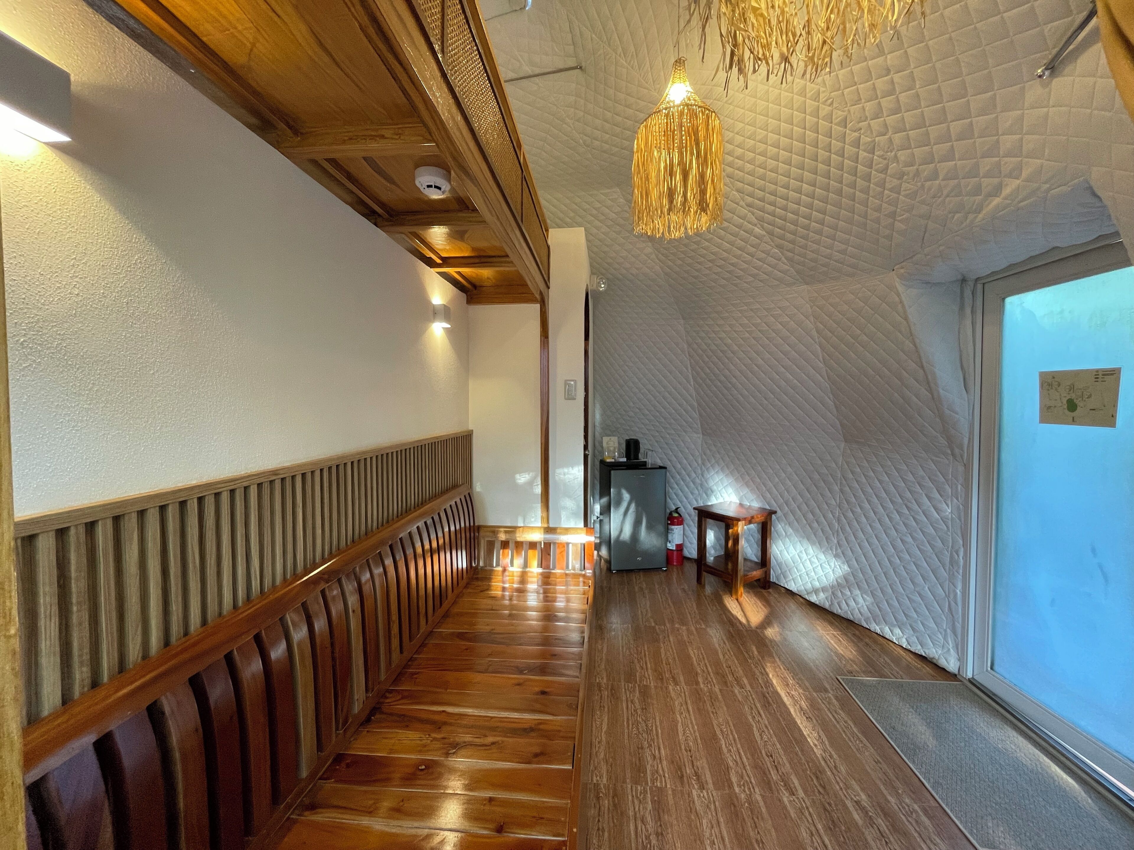 A hallway with wooden flooring, a bench, a hanging light fixture, and a door with a window.