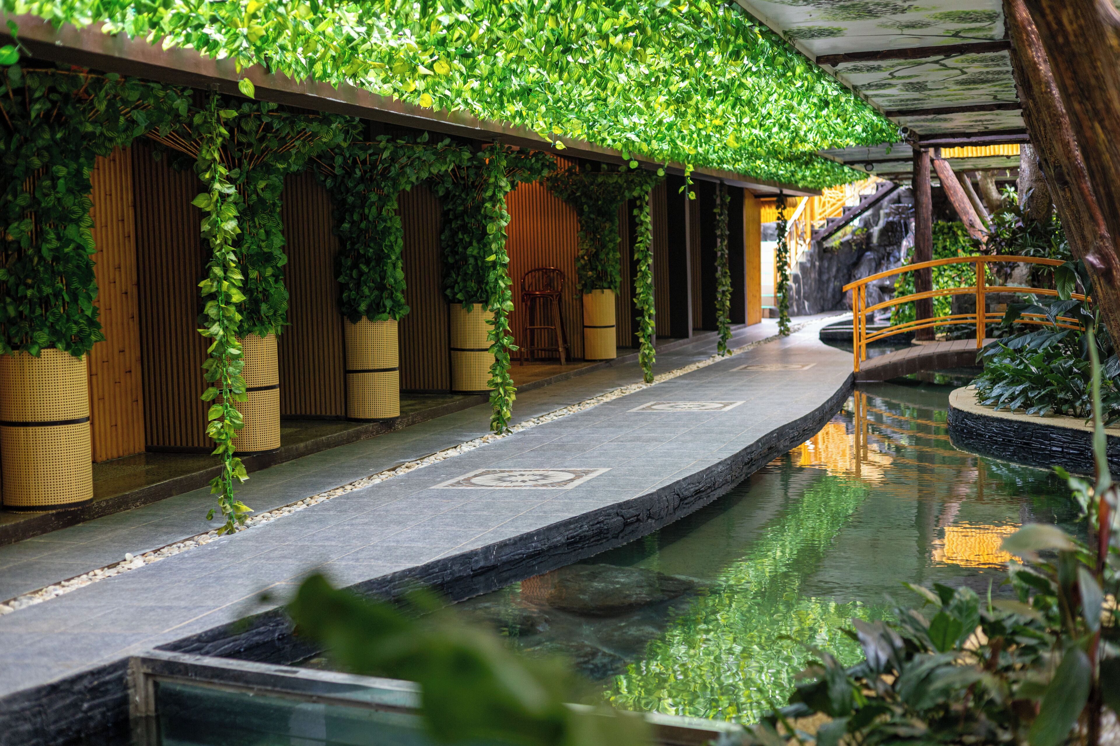 Une piscine intérieure dotée d’une terrasse en bois, d’un pont et d’une végétation luxuriante.