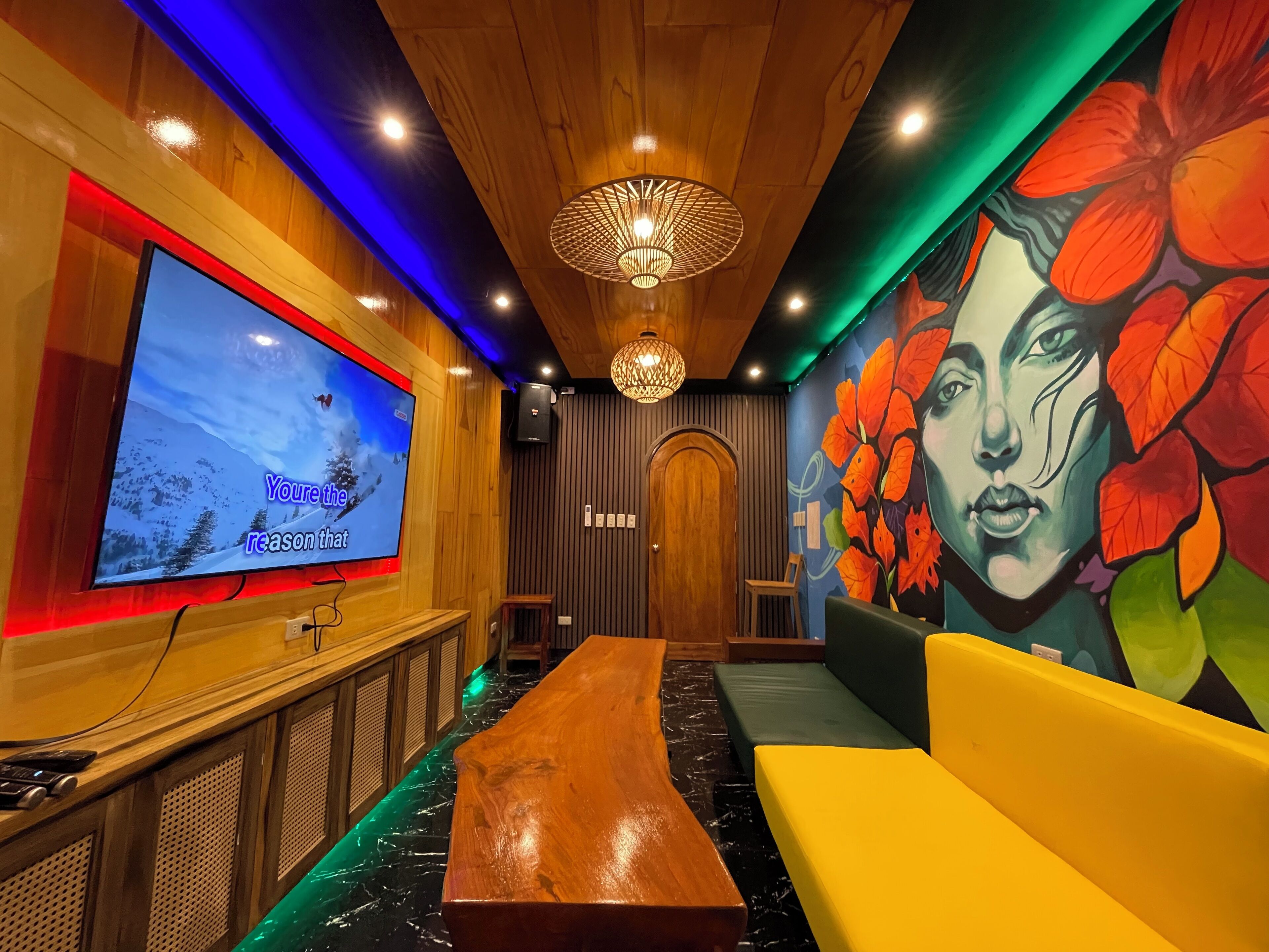 Una habitación con techo de madera, un televisor de pantalla plana grande, un banco, un sofá y un mural en la pared.