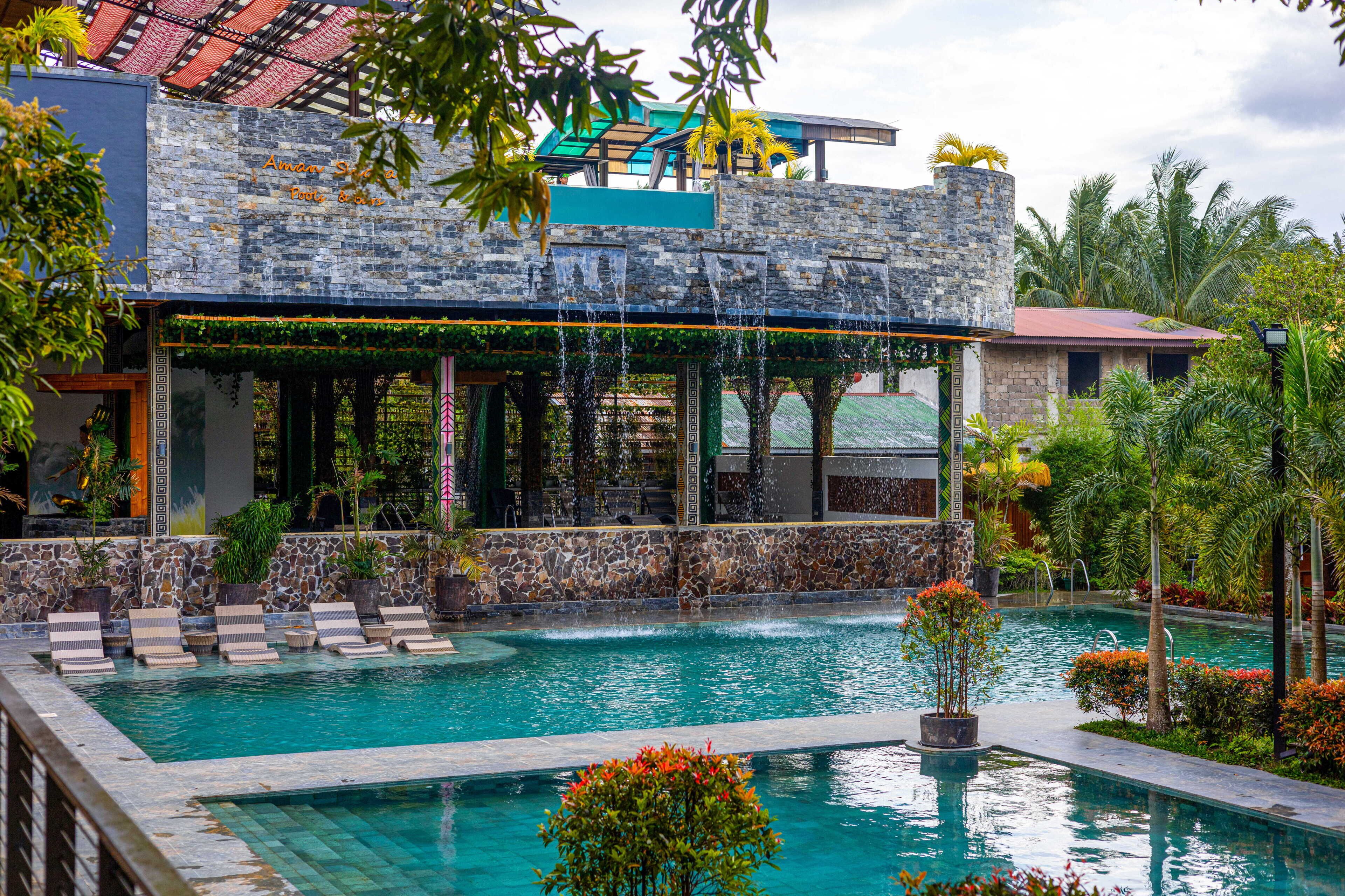 A pool area with lounge chairs, a stone building, and tropical plants.