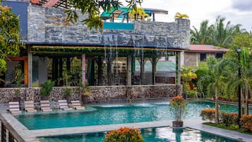 A pool area with lounge chairs, a stone building, and tropical plants.